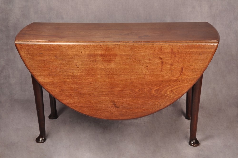 An 18th-century mahogany drop-leaf gateleg table with tapered legs, pad feet, and a scalloped apron on a plain background. View IV