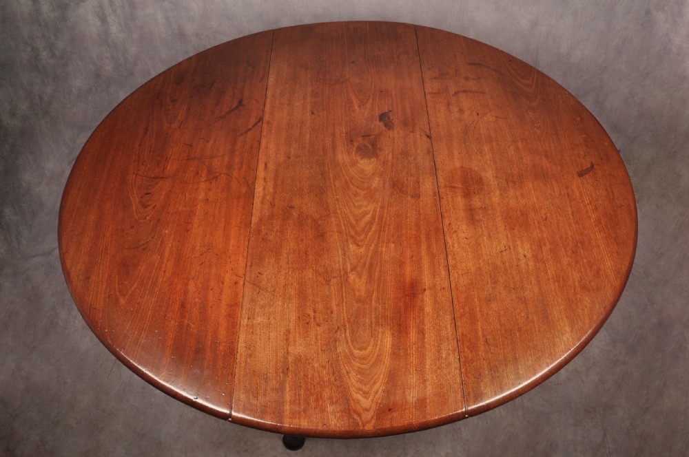 An 18th-century mahogany drop-leaf gateleg table with tapered legs, pad feet, and a scalloped apron on a plain background. View V