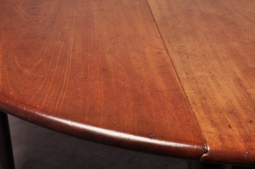 An 18th-century mahogany drop-leaf gateleg table with tapered legs, pad feet, and a scalloped apron on a plain background. View VI