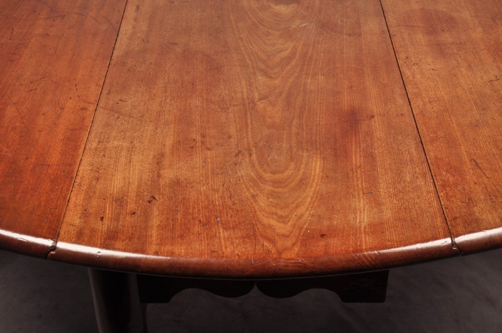 An 18th-century mahogany drop-leaf gateleg table with tapered legs, pad feet, and a scalloped apron on a plain background. View VII