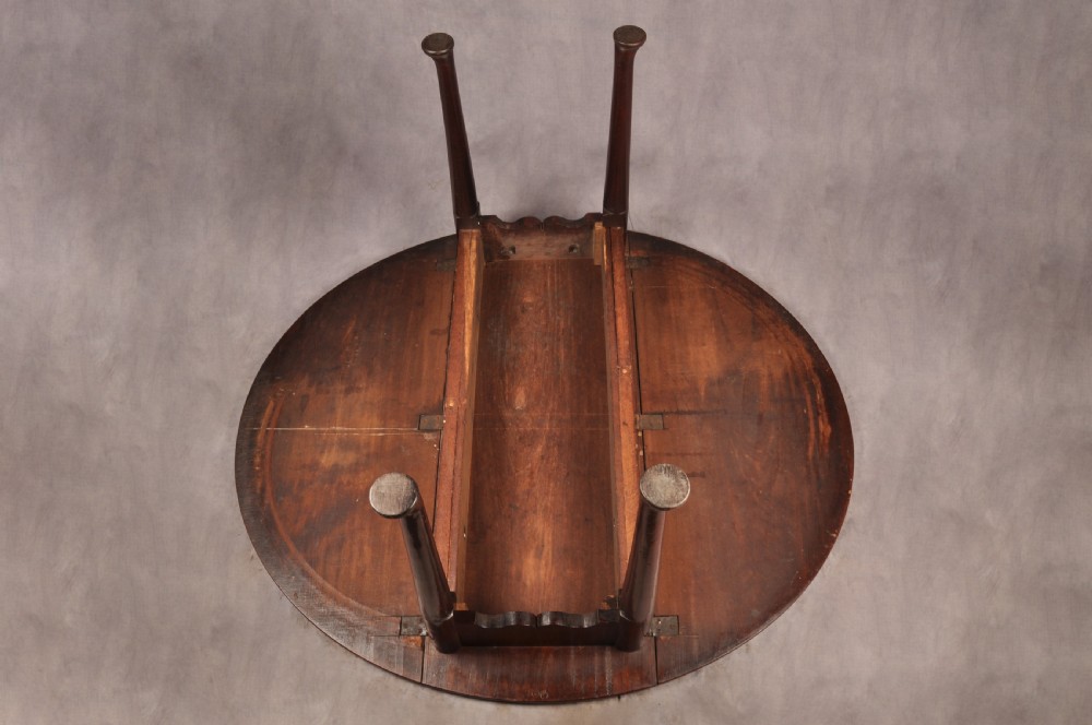 An 18th-century mahogany drop-leaf gateleg table with tapered legs, pad feet, and a scalloped apron on a plain background. View IX