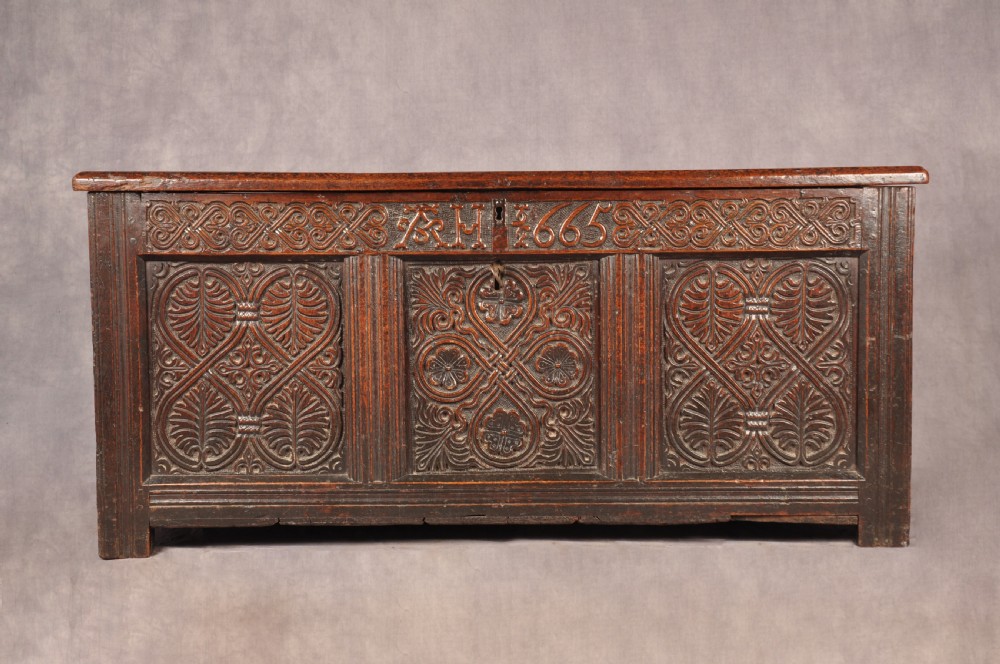 A dark 17th-century oak coffer with three relief-carved front panels and a top frieze inscribed with the initials TH and date 1665.