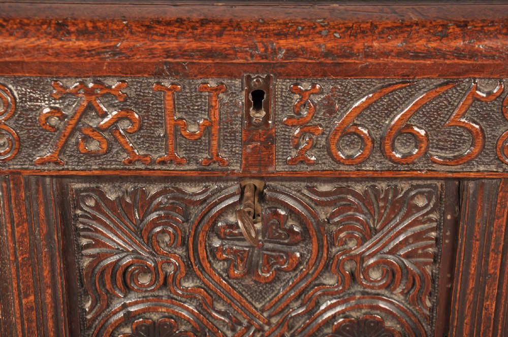 A dark 17th-century oak coffer with three relief-carved front panels and a top frieze inscribed with the initials TH and date 1665. View IV