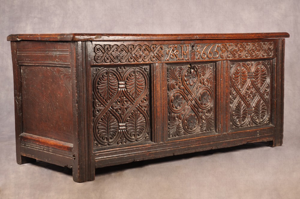 A dark 17th-century oak coffer with three relief-carved front panels and a top frieze inscribed with the initials TH and date 1665. View V