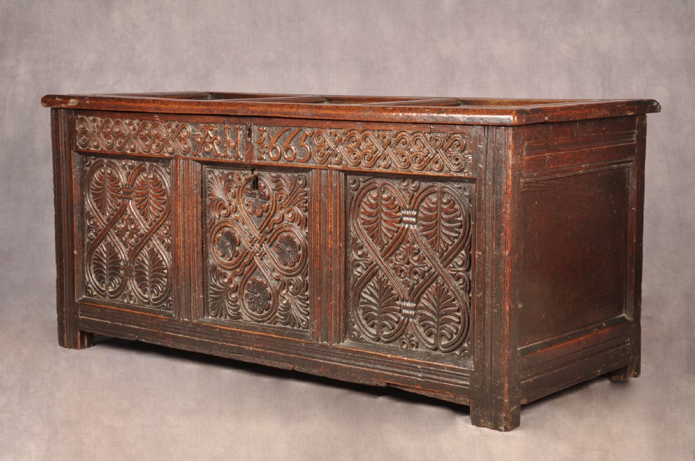 A dark 17th-century oak coffer with three relief-carved front panels and a top frieze inscribed with the initials TH and date 1665. View VI