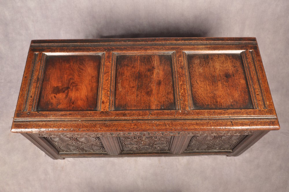 A dark 17th-century oak coffer with three relief-carved front panels and a top frieze inscribed with the initials TH and date 1665. View VII
