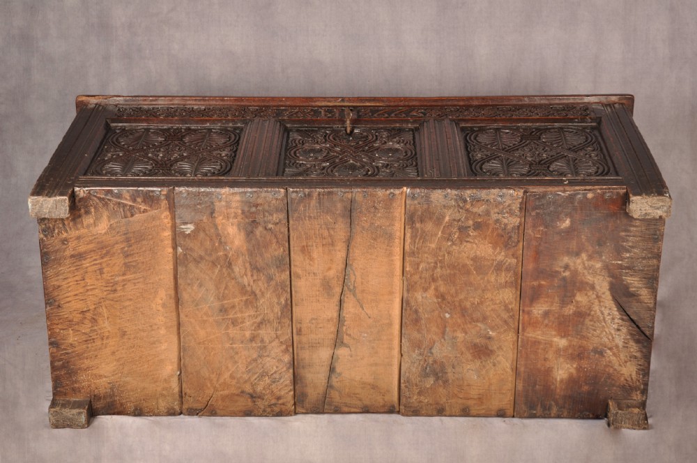A dark 17th-century oak coffer with three relief-carved front panels and a top frieze inscribed with the initials TH and date 1665. View X