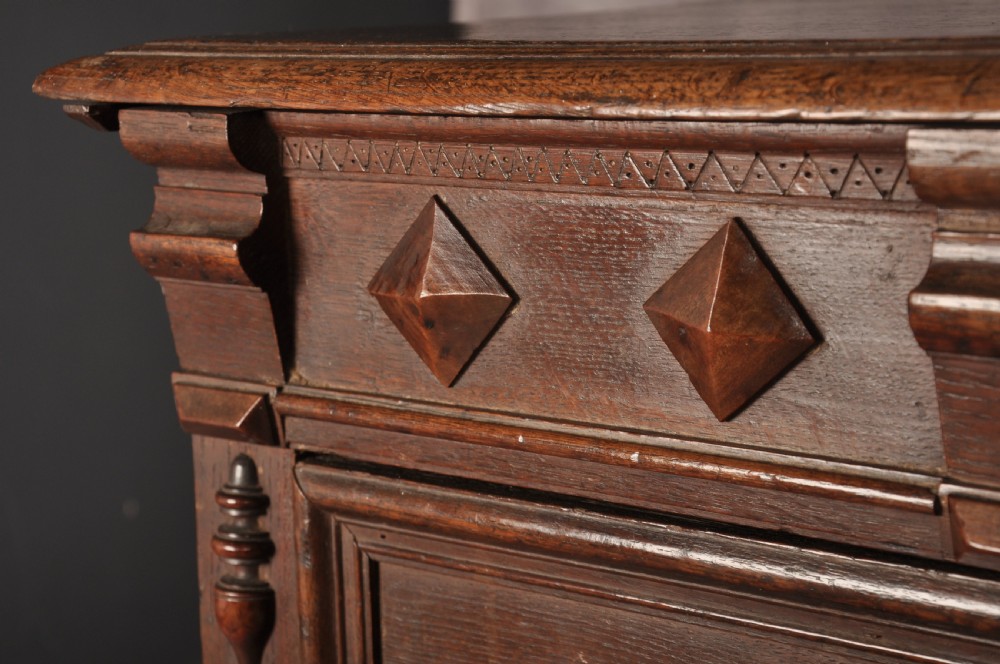 A 17th-century dark oak chest of drawers featuring geometric mouldings, split baluster details, brass drop handles, and a scalloped apron. View II