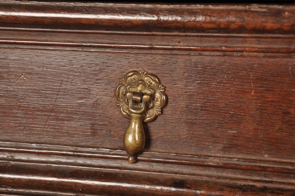 A 17th-century dark oak chest of drawers featuring geometric mouldings, split baluster details, brass drop handles, and a scalloped apron. View V