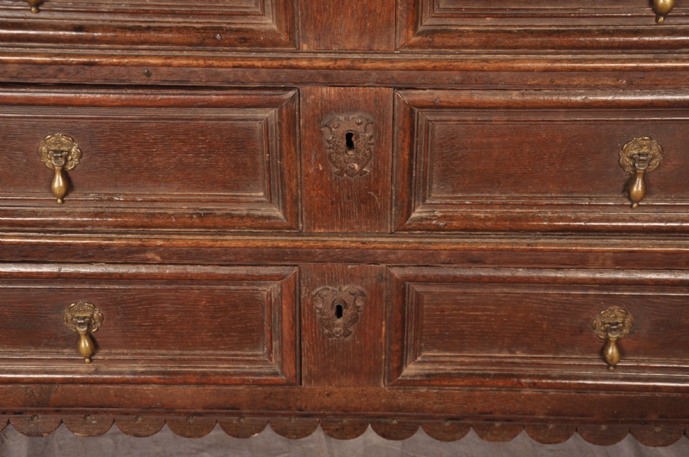 A 17th-century dark oak chest of drawers featuring geometric mouldings, split baluster details, brass drop handles, and a scalloped apron. View VI
