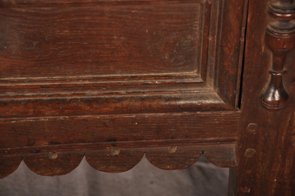 A 17th-century dark oak chest of drawers featuring geometric mouldings, split baluster details, brass drop handles, and a scalloped apron. View VII
