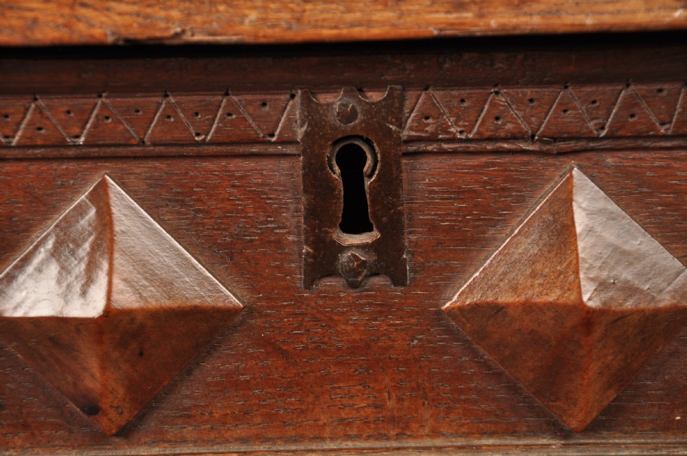 A 17th-century dark oak chest of drawers featuring geometric mouldings, split baluster details, brass drop handles, and a scalloped apron. View IX