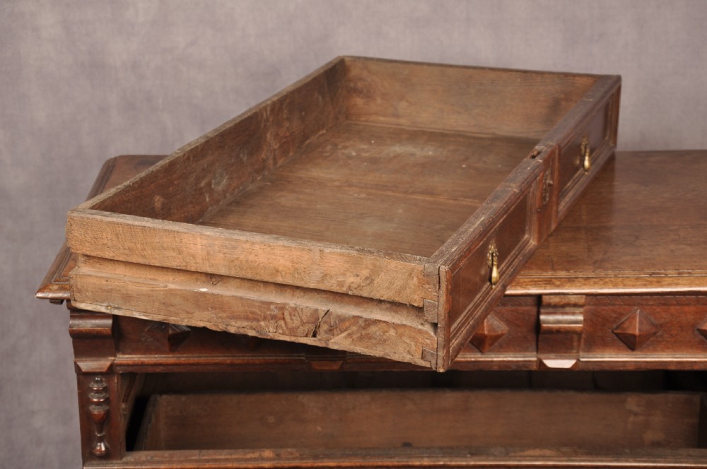 A 17th-century dark oak chest of drawers featuring geometric mouldings, split baluster details, brass drop handles, and a scalloped apron. View XI
