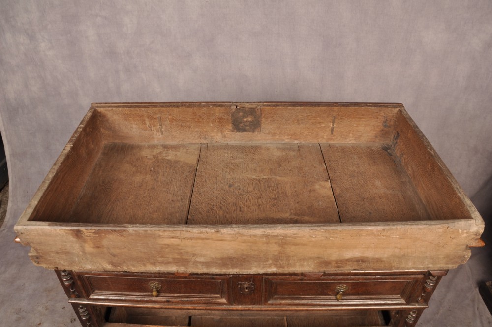 A 17th-century dark oak chest of drawers featuring geometric mouldings, split baluster details, brass drop handles, and a scalloped apron. View XIII