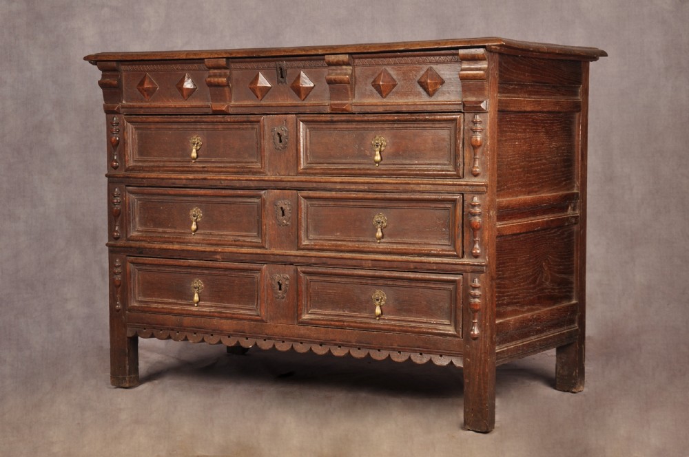A 17th-century dark oak chest of drawers featuring geometric mouldings, split baluster details, brass drop handles, and a scalloped apron. View XX
