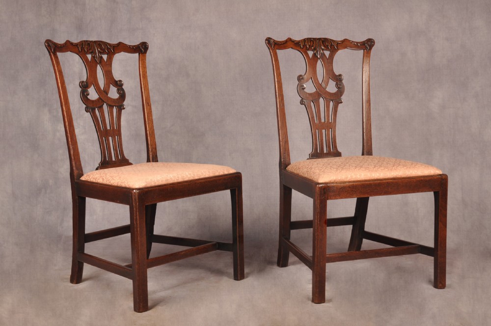 A pair of 18th-century mahogany Chippendale side chairs featuring carved pierced back splats and light patterned upholstered seat pads.