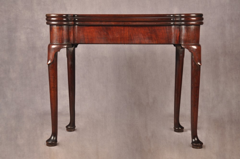 An 18th-century dark mahogany triple-top card table with shaped cabriole legs ending in pad feet.