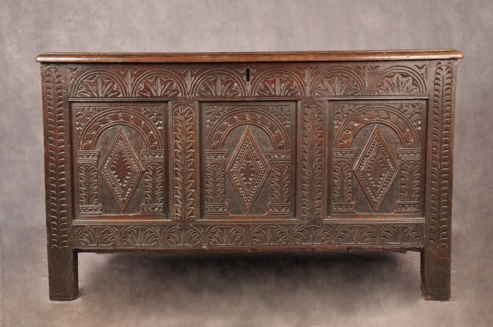 A 17th-century dark oak coffer featuring three carved arcaded panels with central diamond lozenge designs and carved lunette friezes.