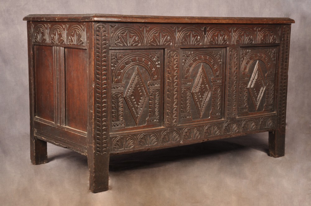 A 17th-century dark oak coffer featuring three carved arcaded panels with central diamond lozenge designs and carved lunette friezes. View II