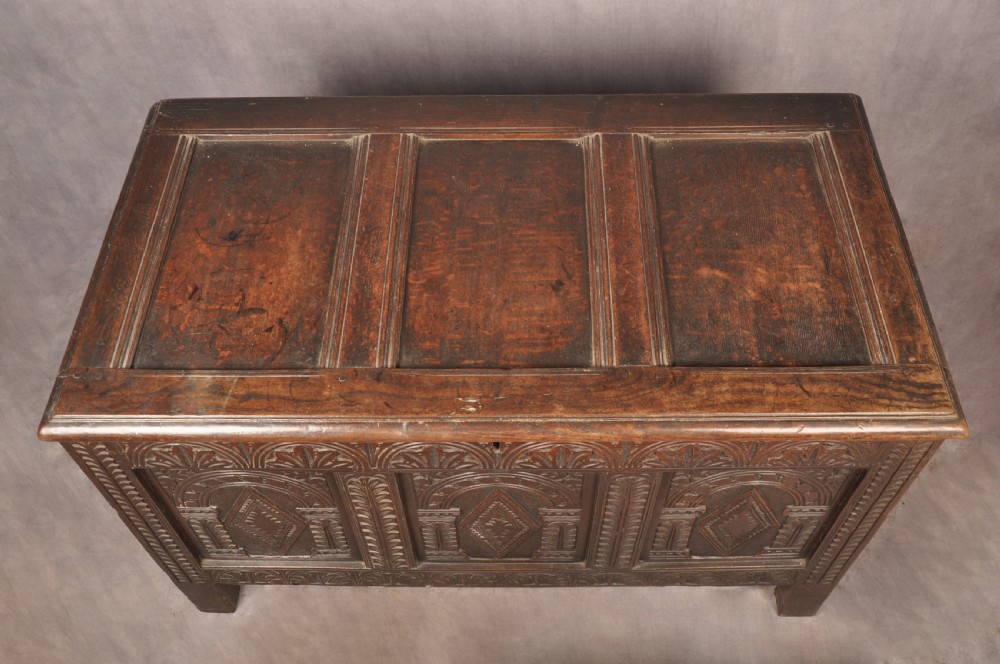 A 17th-century dark oak coffer featuring three carved arcaded panels with central diamond lozenge designs and carved lunette friezes. View IV