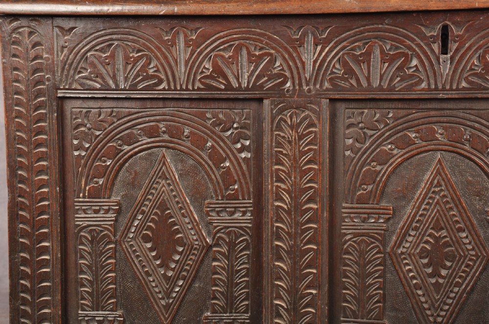 A 17th-century dark oak coffer featuring three carved arcaded panels with central diamond lozenge designs and carved lunette friezes. View VI