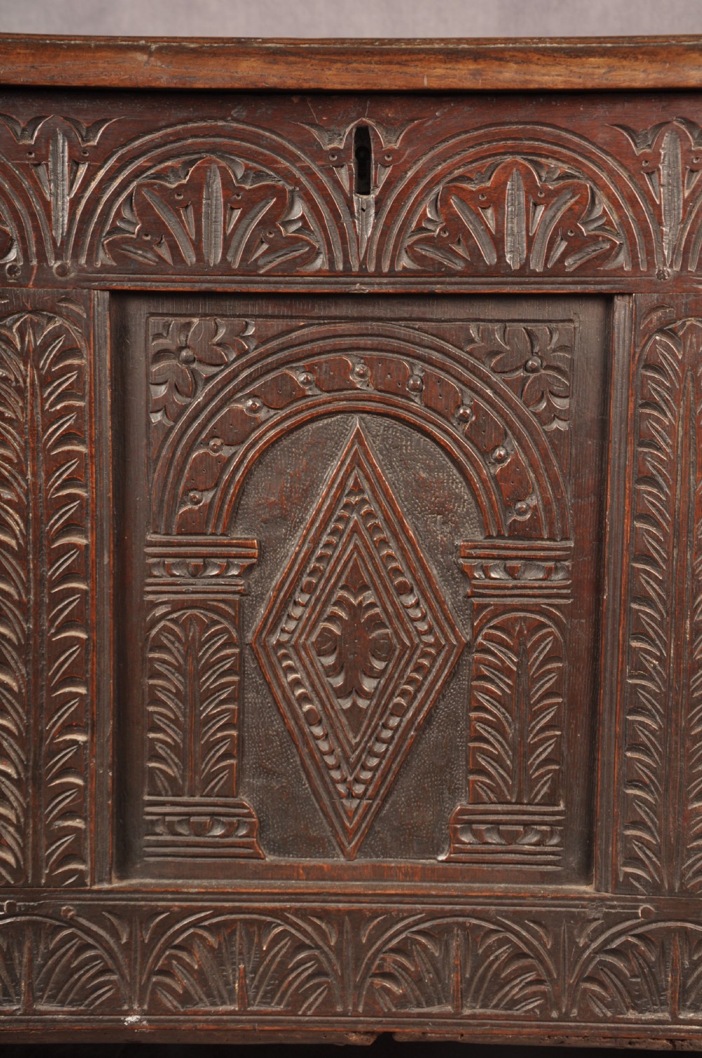 A 17th-century dark oak coffer featuring three carved arcaded panels with central diamond lozenge designs and carved lunette friezes. View VII