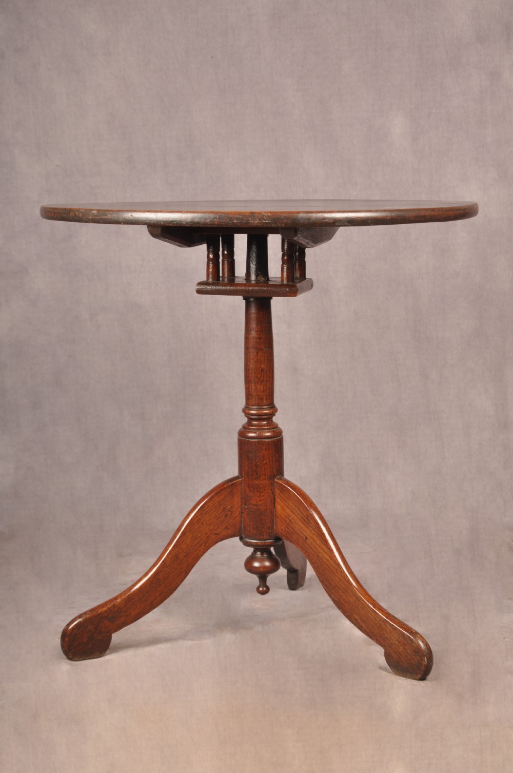 An 18th-century dark oak tripod table featuring a circular top, turned spindle birdcage stem, and three splayed cabriole legs.