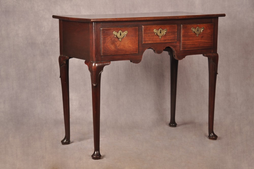 An early 18th-century mahogany lowboy with three drawers, brass handles, a shaped apron, and four cabriole legs with pad feet.