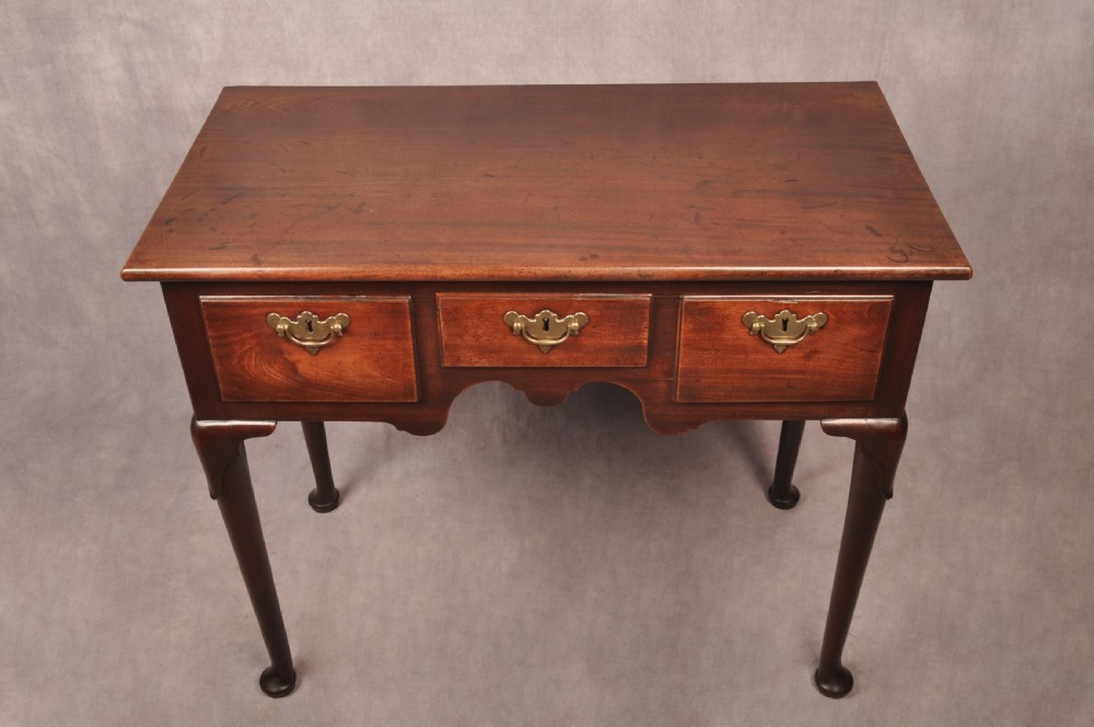 An early 18th-century mahogany lowboy with three drawers, brass handles, a shaped apron, and four cabriole legs with pad feet. View VII