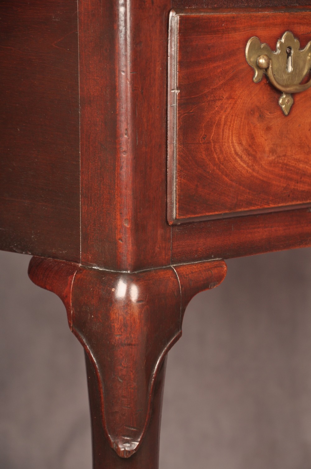 An early 18th-century mahogany lowboy with three drawers, brass handles, a shaped apron, and four cabriole legs with pad feet. View IX