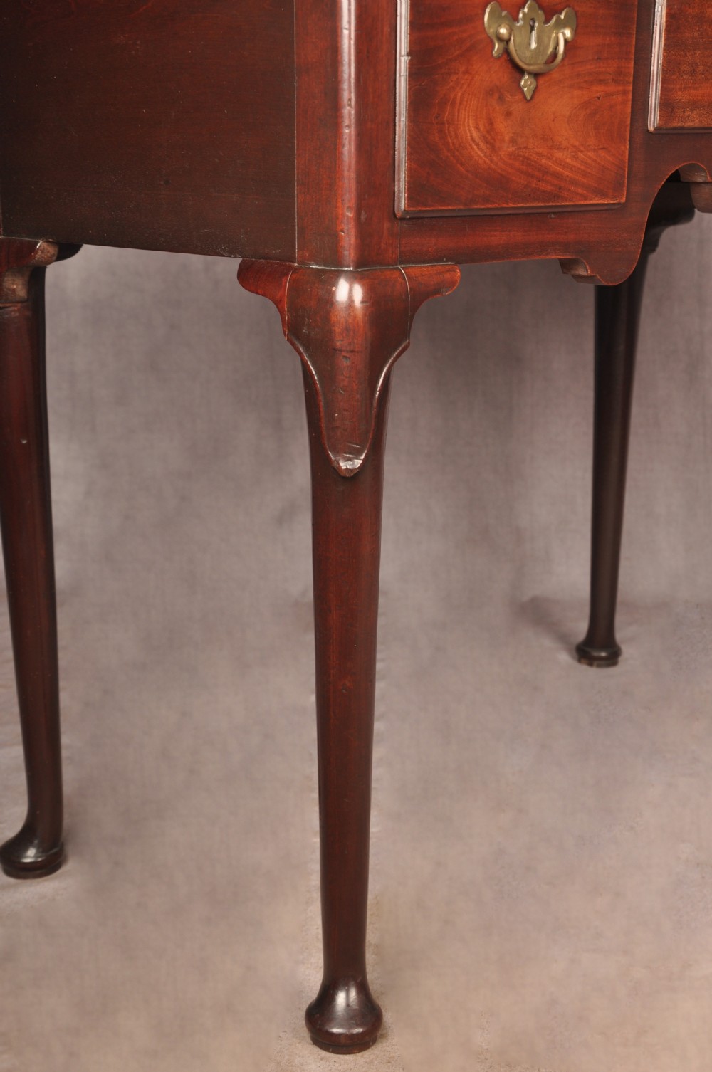 An early 18th-century mahogany lowboy with three drawers, brass handles, a shaped apron, and four cabriole legs with pad feet. View XI
