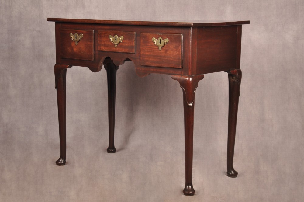 An early 18th-century mahogany lowboy with three drawers, brass handles, a shaped apron, and four cabriole legs with pad feet. View XII