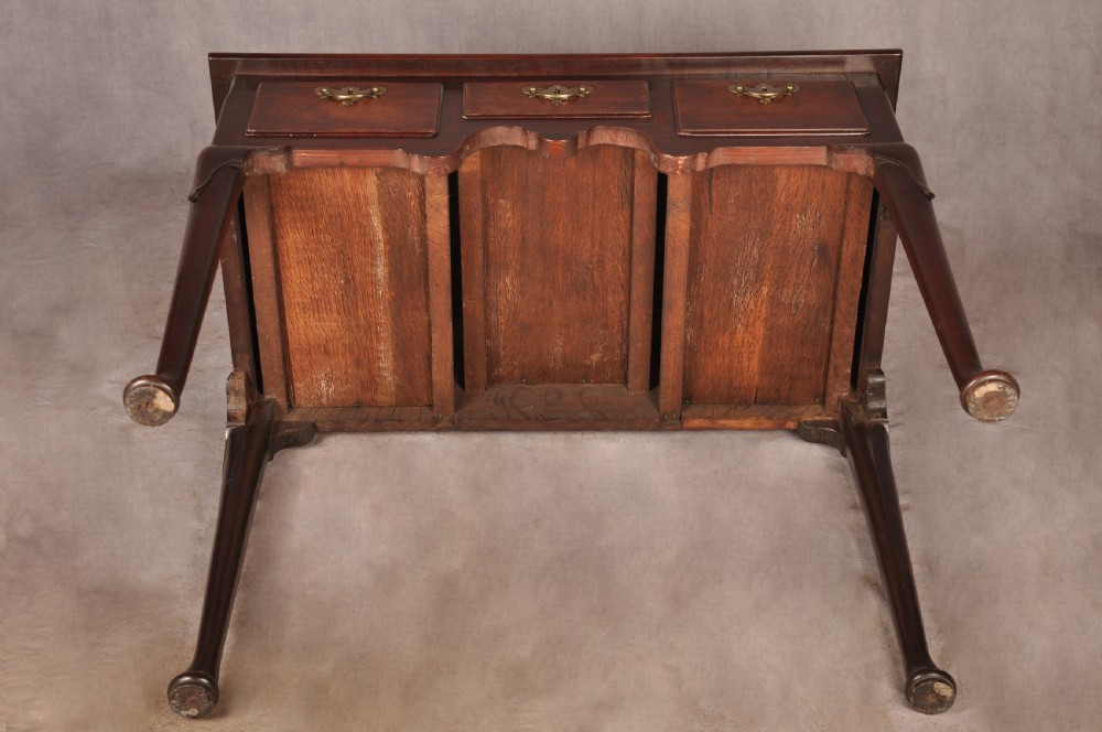 An early 18th-century mahogany lowboy with three drawers, brass handles, a shaped apron, and four cabriole legs with pad feet. View XIV