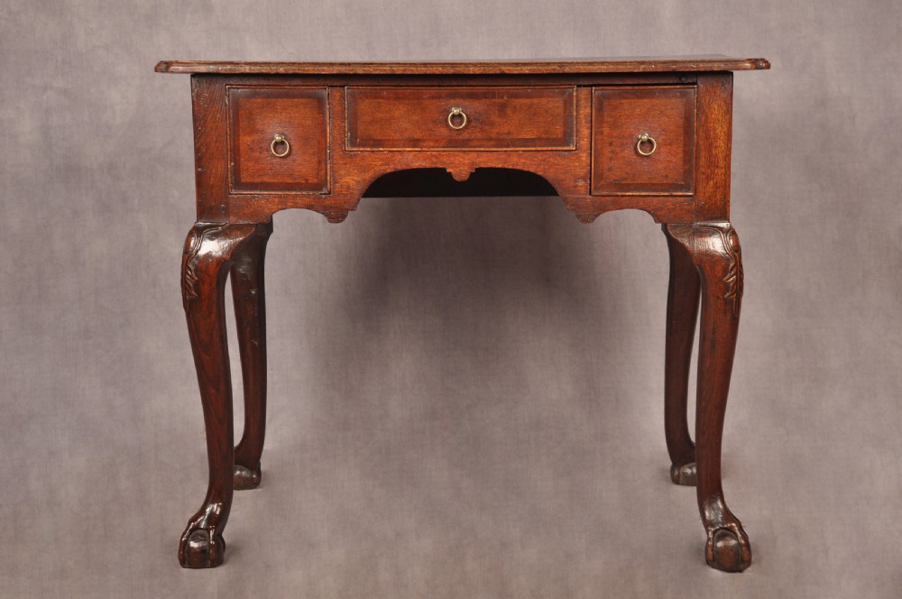 An early 18th-century dark oak lowboy side table featuring three drawers with brass drop handles, a shaped apron, and four cabriole legs.
