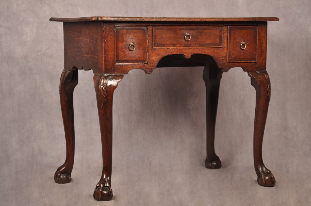 An early 18th-century dark oak lowboy side table featuring three drawers with brass drop handles, a shaped apron, and four cabriole legs. View II