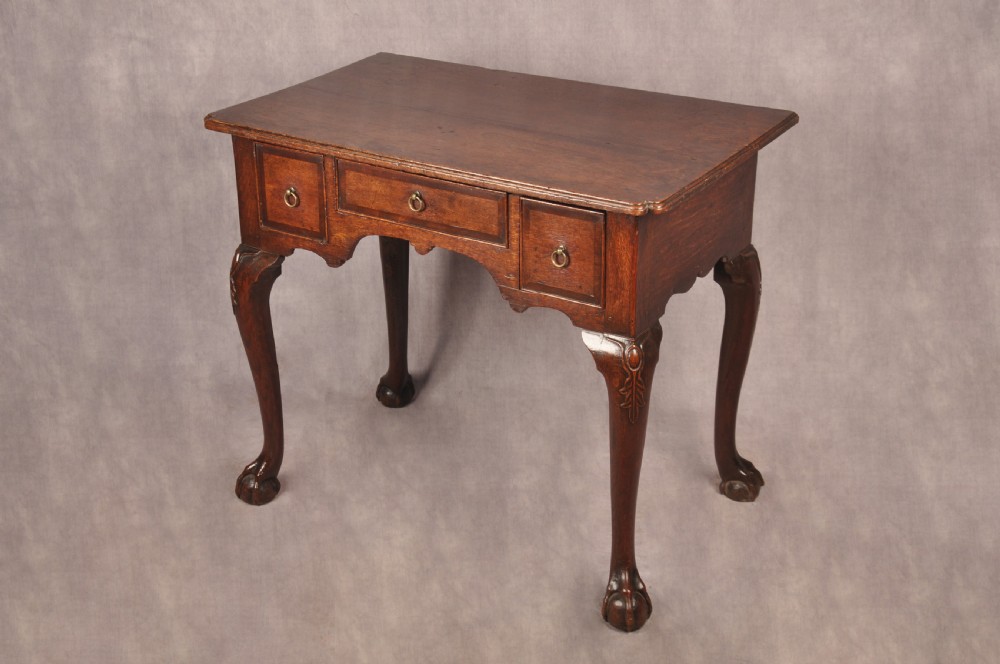 An early 18th-century dark oak lowboy side table featuring three drawers with brass drop handles, a shaped apron, and four cabriole legs. View III