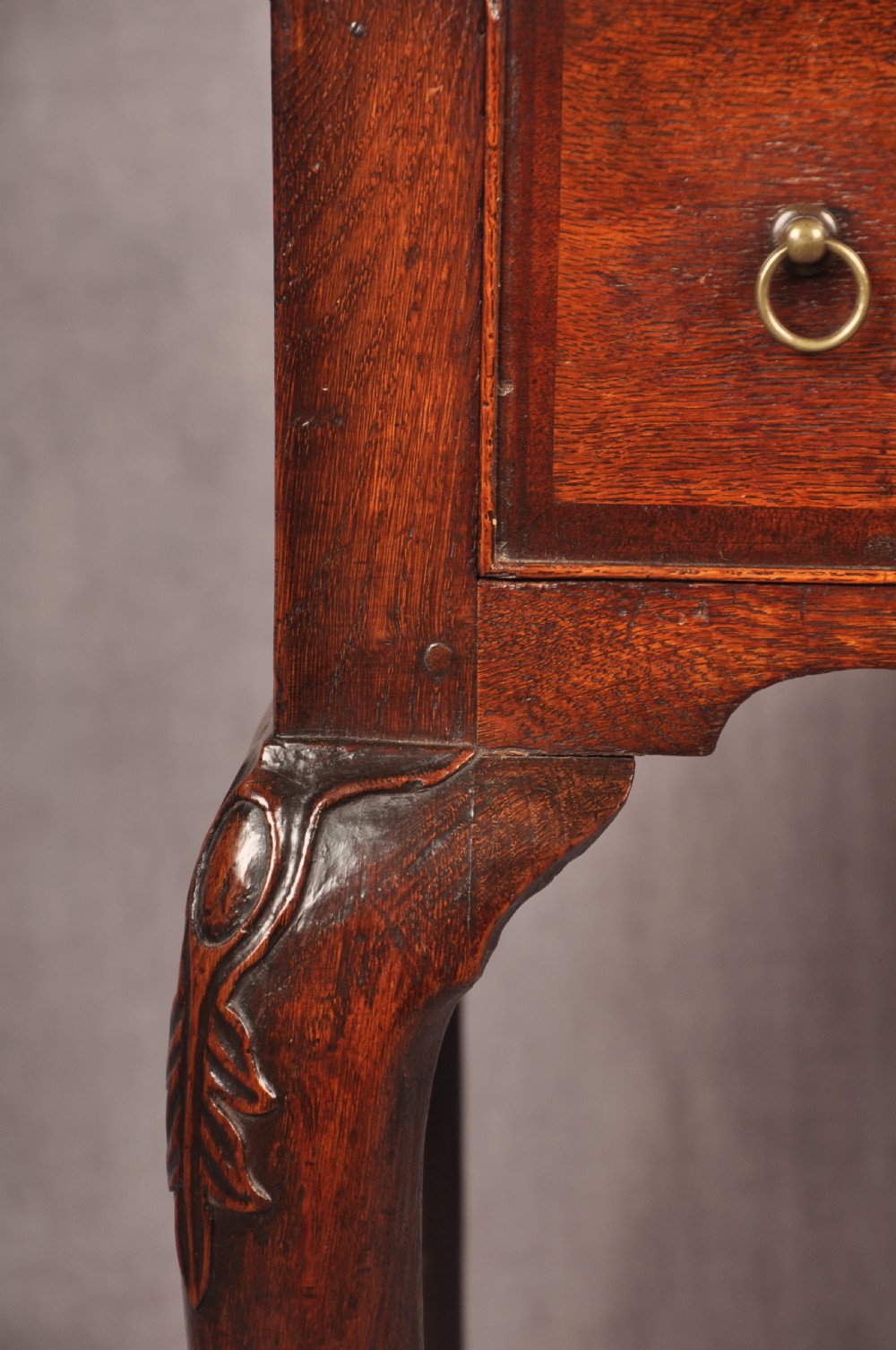 An early 18th-century dark oak lowboy side table featuring three drawers with brass drop handles, a shaped apron, and four cabriole legs. View IV