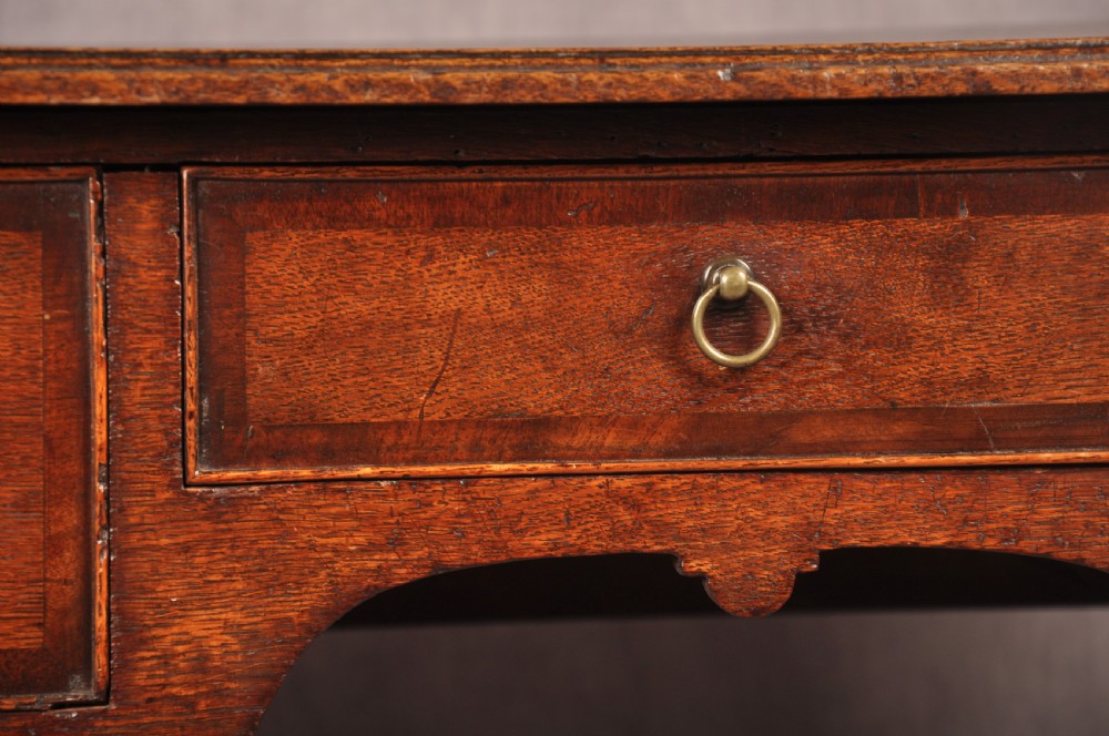 An early 18th-century dark oak lowboy side table featuring three drawers with brass drop handles, a shaped apron, and four cabriole legs. View V