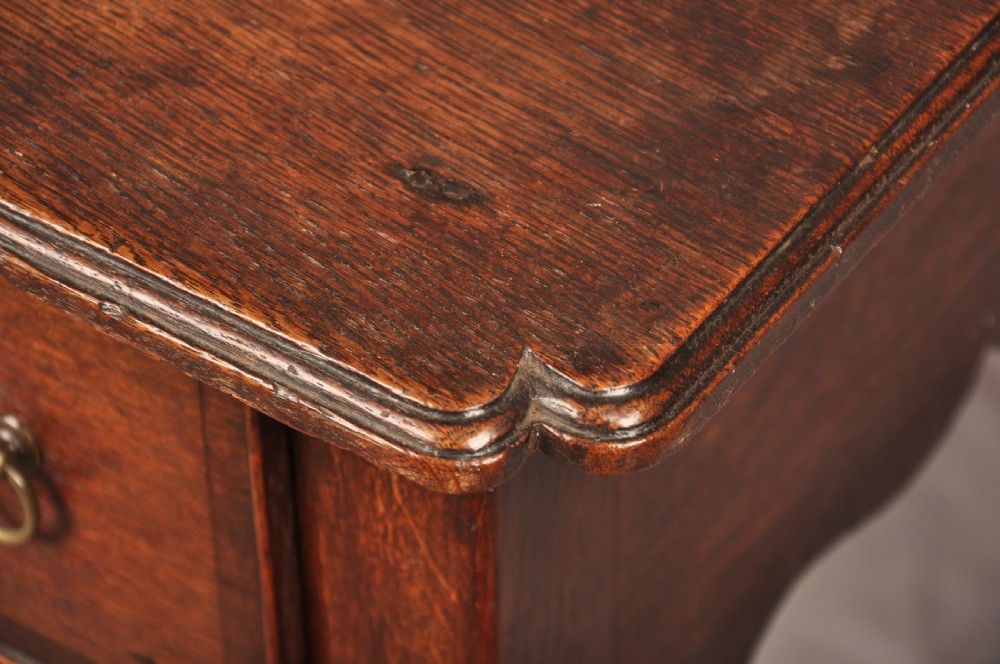 An early 18th-century dark oak lowboy side table featuring three drawers with brass drop handles, a shaped apron, and four cabriole legs. View XV