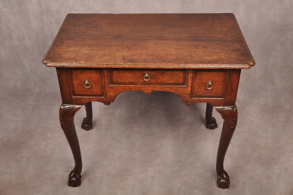 An early 18th-century dark oak lowboy side table featuring three drawers with brass drop handles, a shaped apron, and four cabriole legs. View XVII