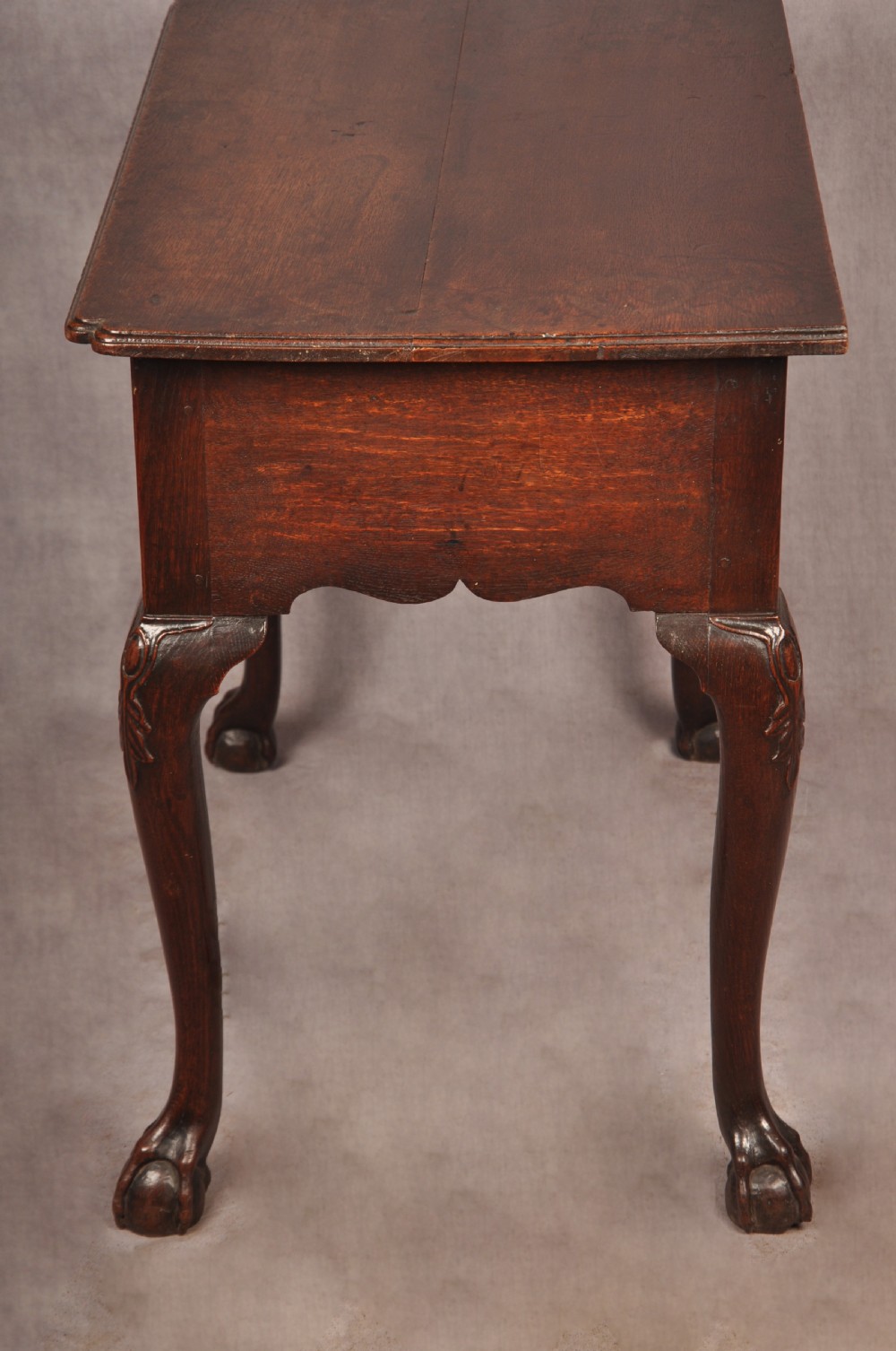 An early 18th-century dark oak lowboy side table featuring three drawers with brass drop handles, a shaped apron, and four cabriole legs. View XVIII