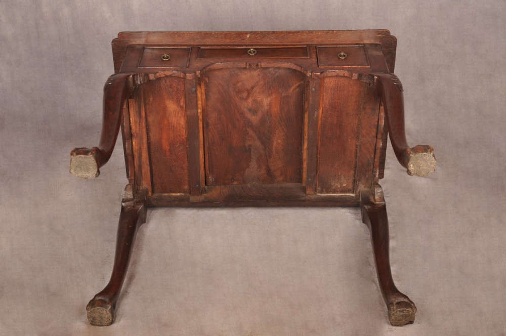 An early 18th-century dark oak lowboy side table featuring three drawers with brass drop handles, a shaped apron, and four cabriole legs. View XIX