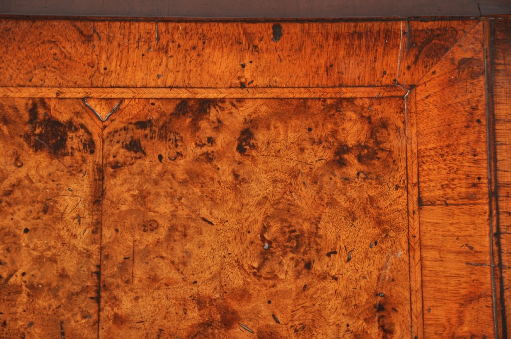 An early 18th-century burr walnut slant-front bureau featuring brass drop handles, keyhole escutcheons, and a chest of drawers base. View III