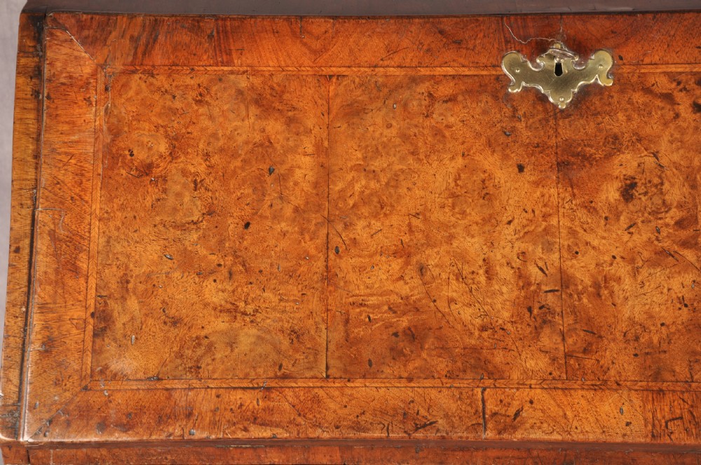 An early 18th-century burr walnut slant-front bureau featuring brass drop handles, keyhole escutcheons, and a chest of drawers base. View IV