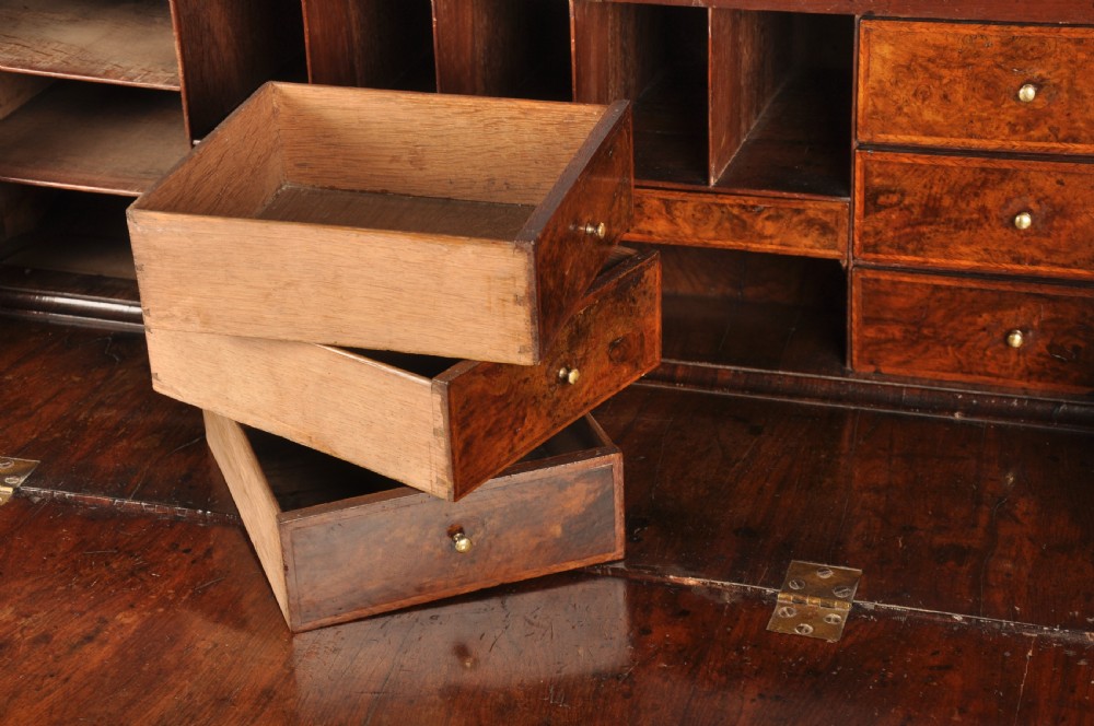 An early 18th-century burr walnut slant-front bureau featuring brass drop handles, keyhole escutcheons, and a chest of drawers base. View VI