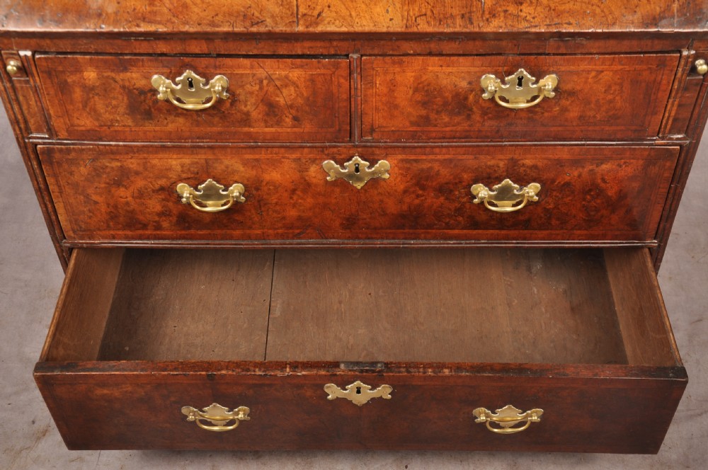 An early 18th-century burr walnut slant-front bureau featuring brass drop handles, keyhole escutcheons, and a chest of drawers base. View VII