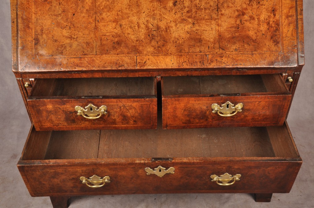 An early 18th-century burr walnut slant-front bureau featuring brass drop handles, keyhole escutcheons, and a chest of drawers base. View VIII