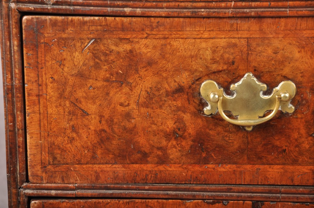 An early 18th-century burr walnut slant-front bureau featuring brass drop handles, keyhole escutcheons, and a chest of drawers base. View IX