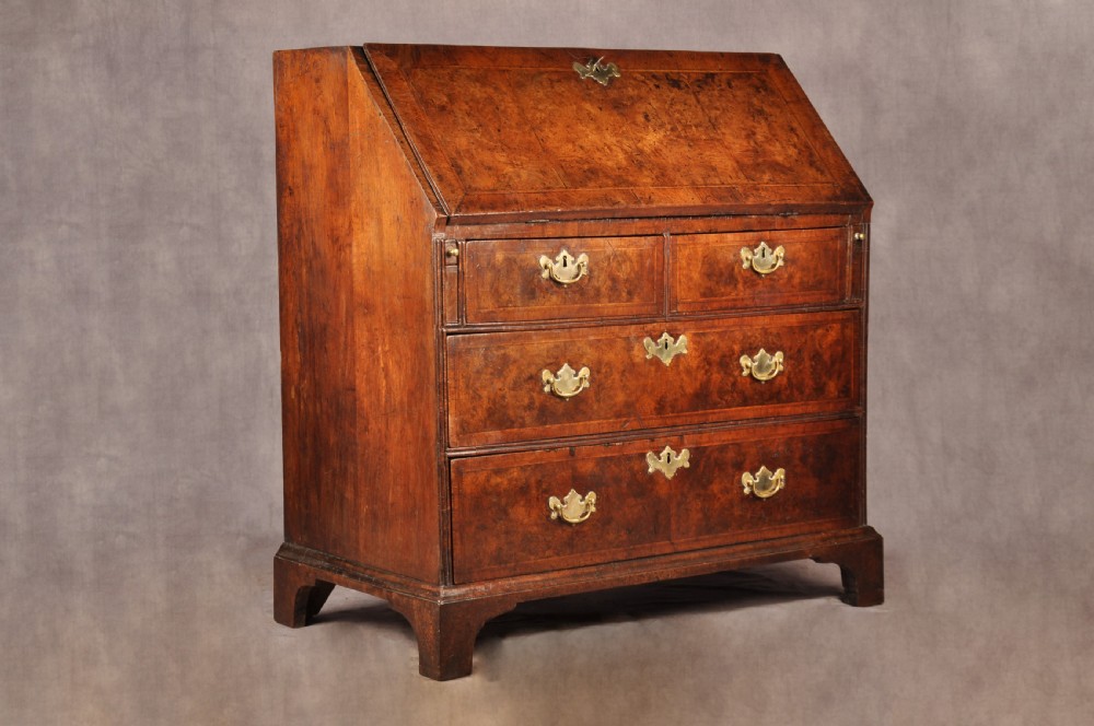 An early 18th-century burr walnut slant-front bureau featuring brass drop handles, keyhole escutcheons, and a chest of drawers base. View XIV