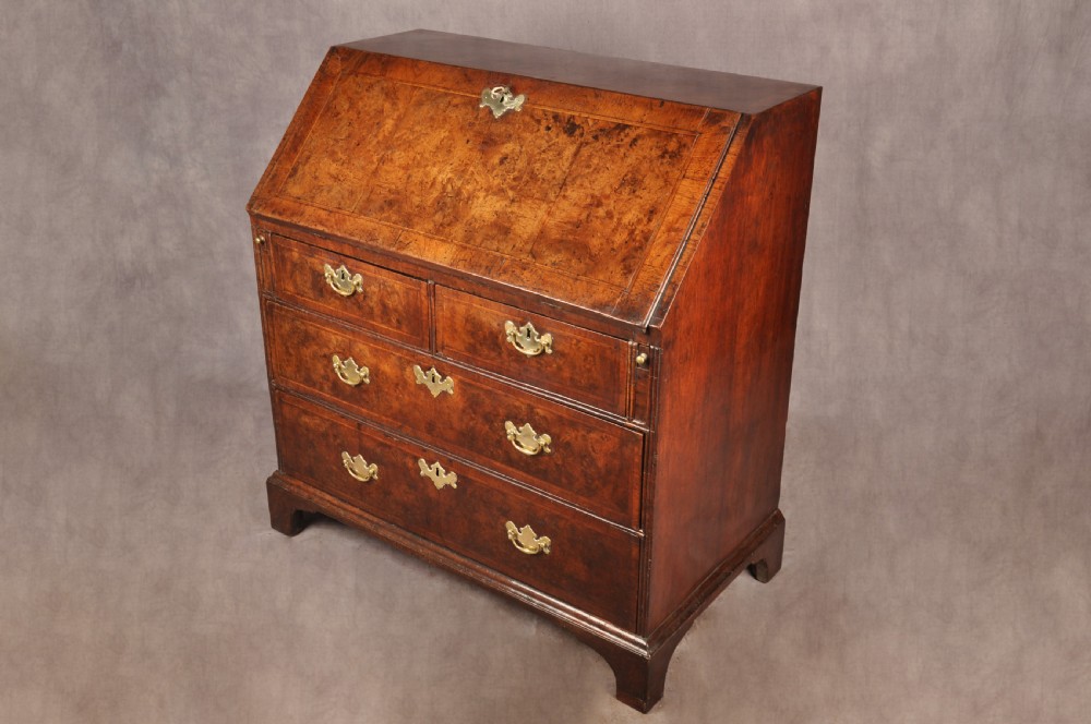 An early 18th-century burr walnut slant-front bureau featuring brass drop handles, keyhole escutcheons, and a chest of drawers base. View XV